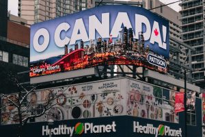 A bustling street in Toronto with a prominent 'O Canada' billboard, cars, and skyscrapers.